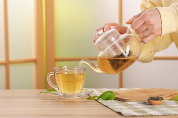 Woman pouring tasty green tea into cup at wooden table indoors, closeup