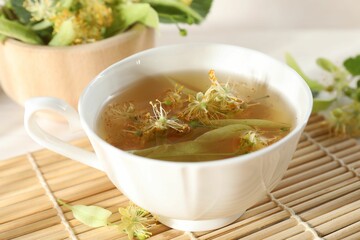 Fresh linden tea in cup and flowers on table, closeup