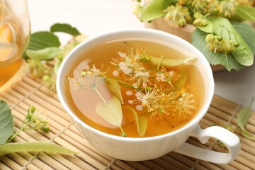 Fresh linden tea in cup, teapot and flowers on white table, closeup
