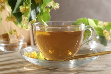 Tasty linden tea in cup, spoon, leaves and flowers on wooden table against grey background, closeup