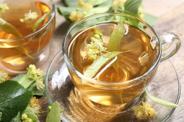 Tasty linden tea in cups, leaves and flowers on wooden table, closeup