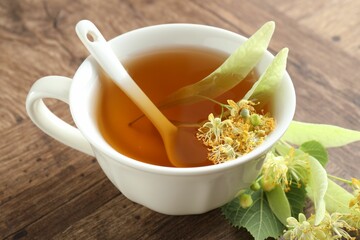 Tasty linden tea in cup, leaves and flowers on wooden table, closeup
