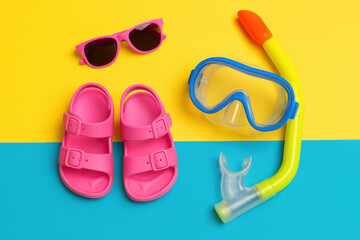 Pink sandals, diving mask, snorkel and sunglasses lying on yellow and blue background