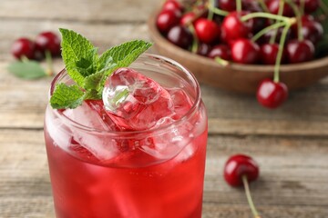 Tasty cherry soda with ice cubes, berries and mint on wooden table, closeup