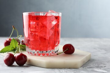 Tasty cherry soda with ice cubes, berries and mint in glass on grey textured table, closeup. Space...