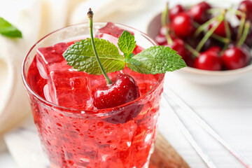 Tasty cherry soda with ice cubes, berries and mint in glass on white wooden table, closeup