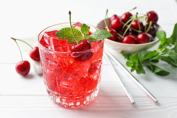 Tasty cherry soda with ice cubes, berries and mint in glass on white wooden table, closeup