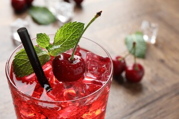 Tasty cherry soda with ice cubes, berries and mint in glass on wooden table, closeup. Space for text