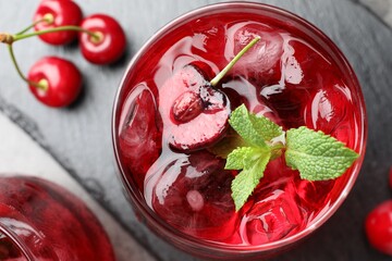 Tasty cherry soda with ice cubes, berries and mint in glasses on grey table, flat lay