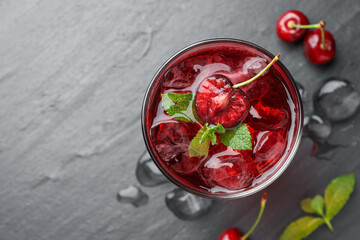 Tasty cherry soda with ice cubes, berries and mint in glass on grey table, flat lay. Space for text