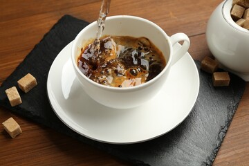 Pouring hot water into cup with instant coffee on wooden table, closeup