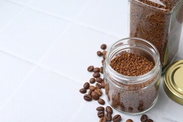 Instant coffee in jars on white tiled table, closeup. Space for text
