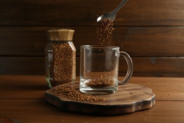 Putting granulated instant coffee into cup on wooden table, closeup