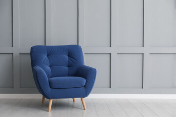 Comfortable blue armchair near light grey wall indoors, space for text