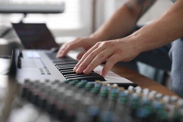 Man working with MIDI keyboard at table indoors, closeup