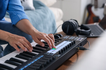 Woman working with MIDI keyboard at table indoors, closeup