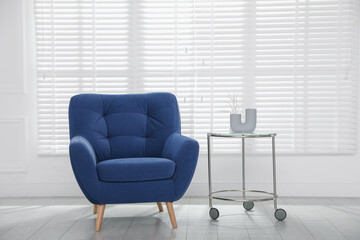 Comfortable blue armchair and side table near white wall indoors