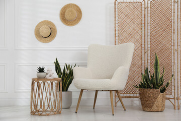 Comfortable armchair, side table and houseplants near white wall indoors