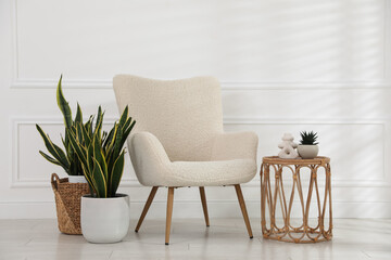 Comfortable armchair, side table and houseplants near white wall indoors
