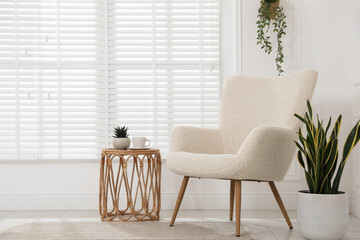 Comfortable armchair, side table and houseplants near white wall indoors