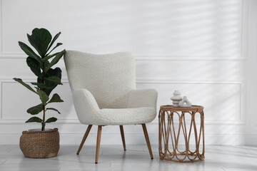 Comfortable armchair, side table and houseplant near white wall indoors