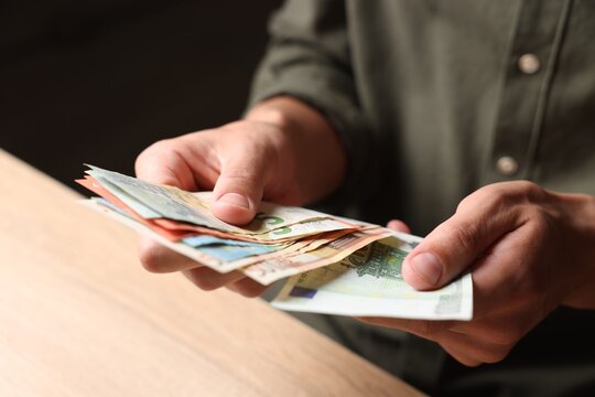 Man counting money at wooden table, closeup