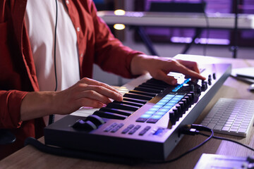 Man working with MIDI keyboard at wooden table indoors, closeup