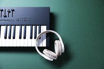 MIDI keyboard and headphones on green background, top view. Space for text