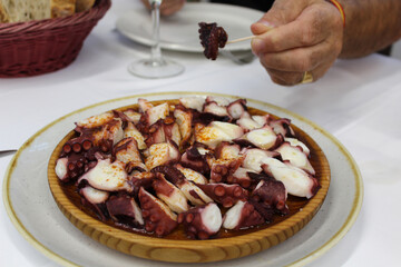 Delicious and irresistible Galician style octopus, served on a wooden plate, sprinkled with smoked paprika, olive oil and coarse salt.