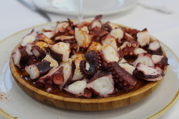 Delicious and irresistible Galician style octopus, served on a wooden plate, sprinkled with smoked paprika, olive oil and coarse salt.