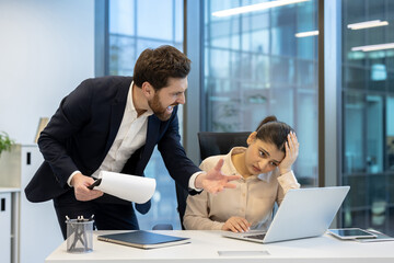 A frustrated businessman yells at his stressed employee while she works on a laptop in a modern office setting.