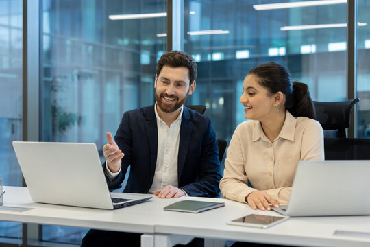 A man and woman in a business meeting at a desk, discussing ideas while looking at a laptop.