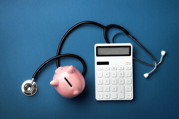 A pink piggy bank with a calculator and stethoscope on blue background. Top view, flat lay.