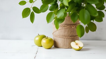 Fresh green apples and lush foliage arranged artfully on a white wooden surface with a burlap wrapped vase