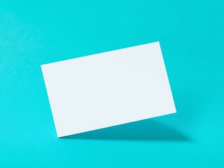 A clean white blank business card floats diagonally on a bright turquoise textured surface creating a minimalist and modern composition
