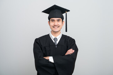 A young man in a graduation gown and cap smiles at the camera, striking a confident pose to...