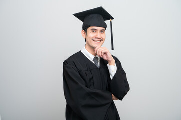 A young man in a graduation gown and cap smiles at the camera, striking a confident pose to...