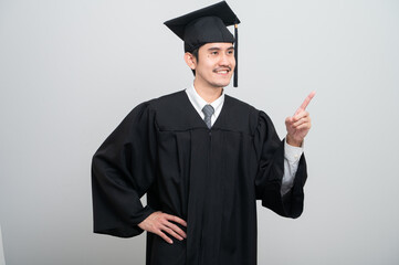 A young man in a graduation gown and cap smiles at the camera, striking a confident pose to...