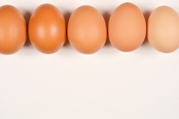 Five brown eggs are perfectly lined up across the top of a simple, light background, providing ample space below for text or design elements