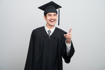A young man in a graduation gown and cap smiles at the camera, striking a confident pose to...