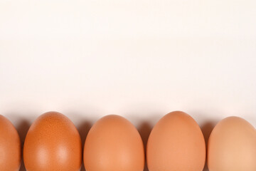 A row of brown eggs is neatly aligned at the bottom of a plain, light-colored background, offering ample copy space above