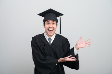 A young man in a graduation gown and cap smiles at the camera, striking a confident pose to...
