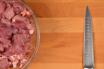 Diced pork pieces in a glass bowl and a knife blade on a wooden cutting board