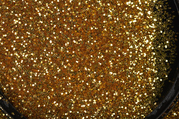 A close-up, high-angle view of dense gold glitter contained within a black, curved edge, creating a vibrant, sparkling texture