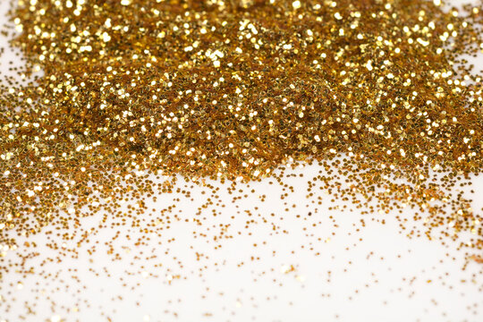 A sparkling close-up of loose gold glitter, piled at the top and scattered across a light surface, creating a festive background
