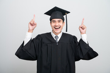 A young man in a graduation gown and cap smiles at the camera, striking a confident pose to...