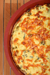 A top-down shot shows a baked cheese and green onion pie with a golden-brown, slightly crispy top in a red baking dish on a wire rack