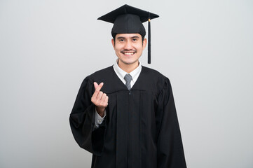 A young man in a graduation gown and cap smiles at the camera, striking a confident pose to...