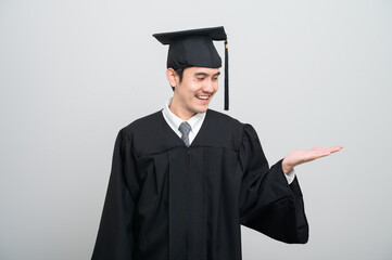 A young man in a graduation gown and cap smiles at the camera, striking a confident pose to...
