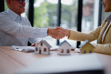 Real estate agent and customer shaking hands after finalizing a contract for a new house,...